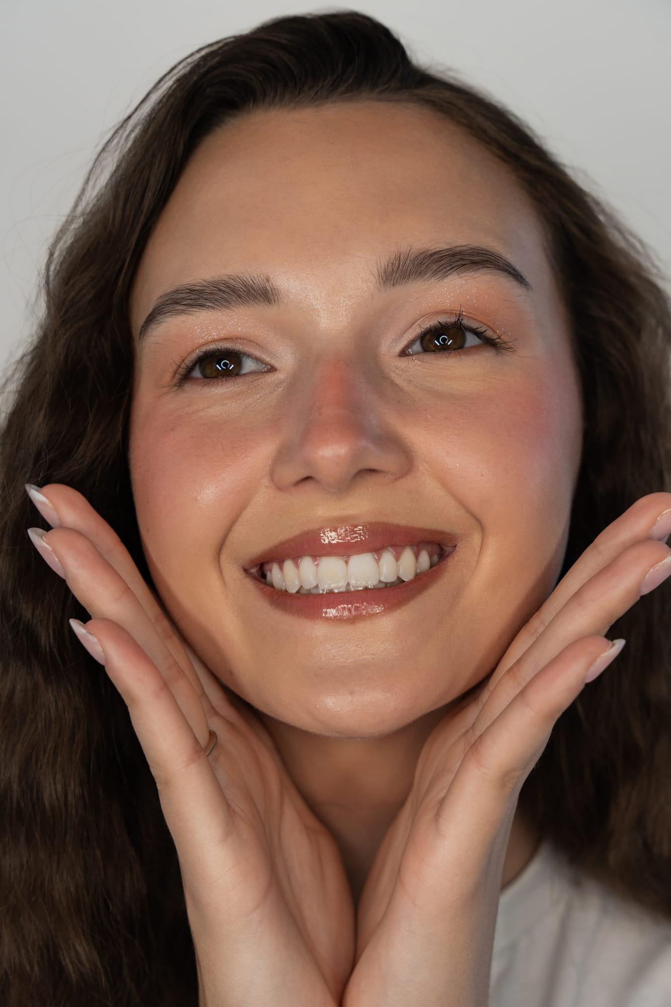 Maquillage naturel, sourire éclatant et mains sur le visage